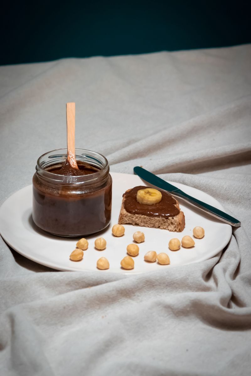 Chocolate nut butter pouring from an open jar onto a wooden board